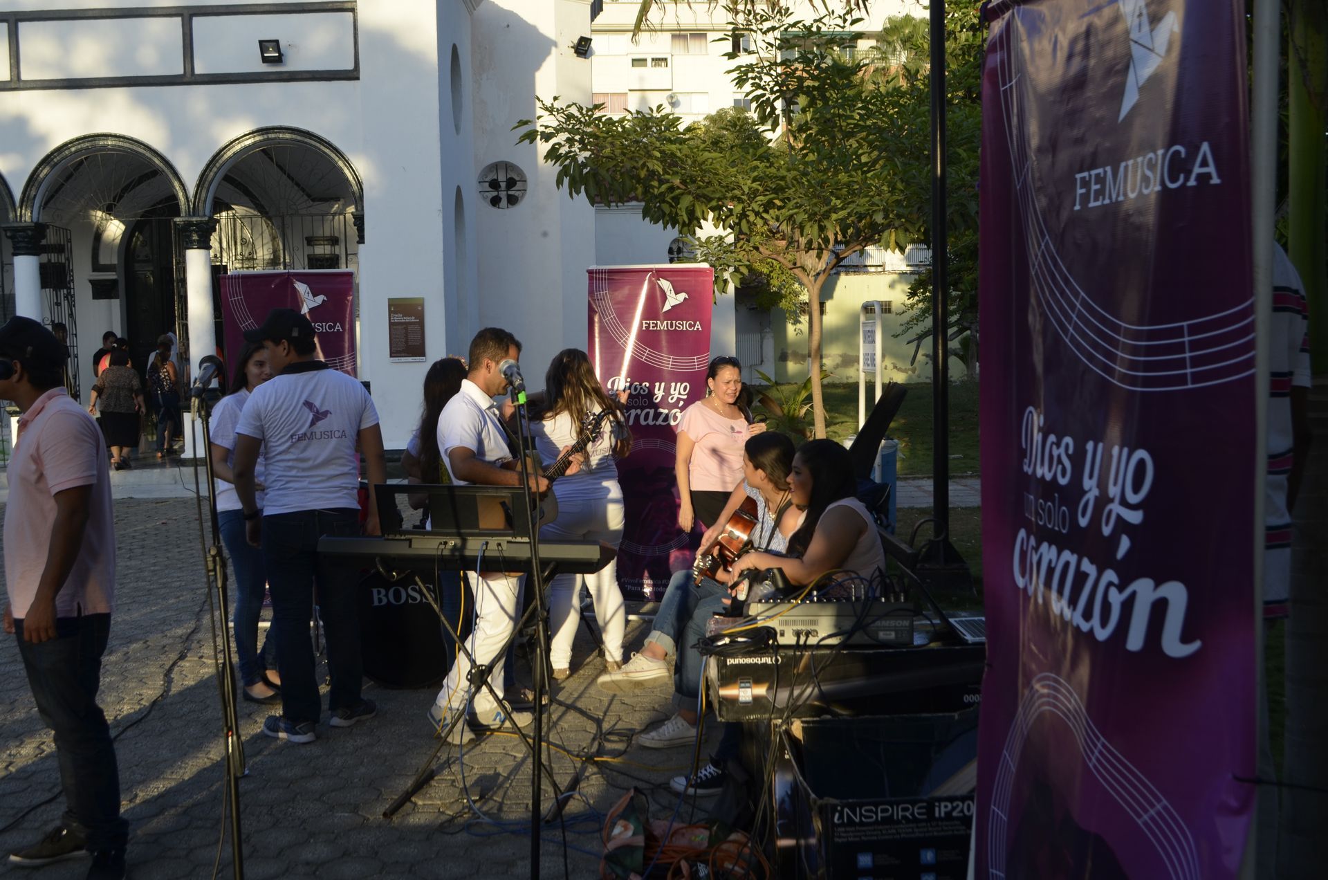 Gente tocando música y reunida frente a un edificio blanco, con pancartas moradas que mostraban textos y motivos musicales.