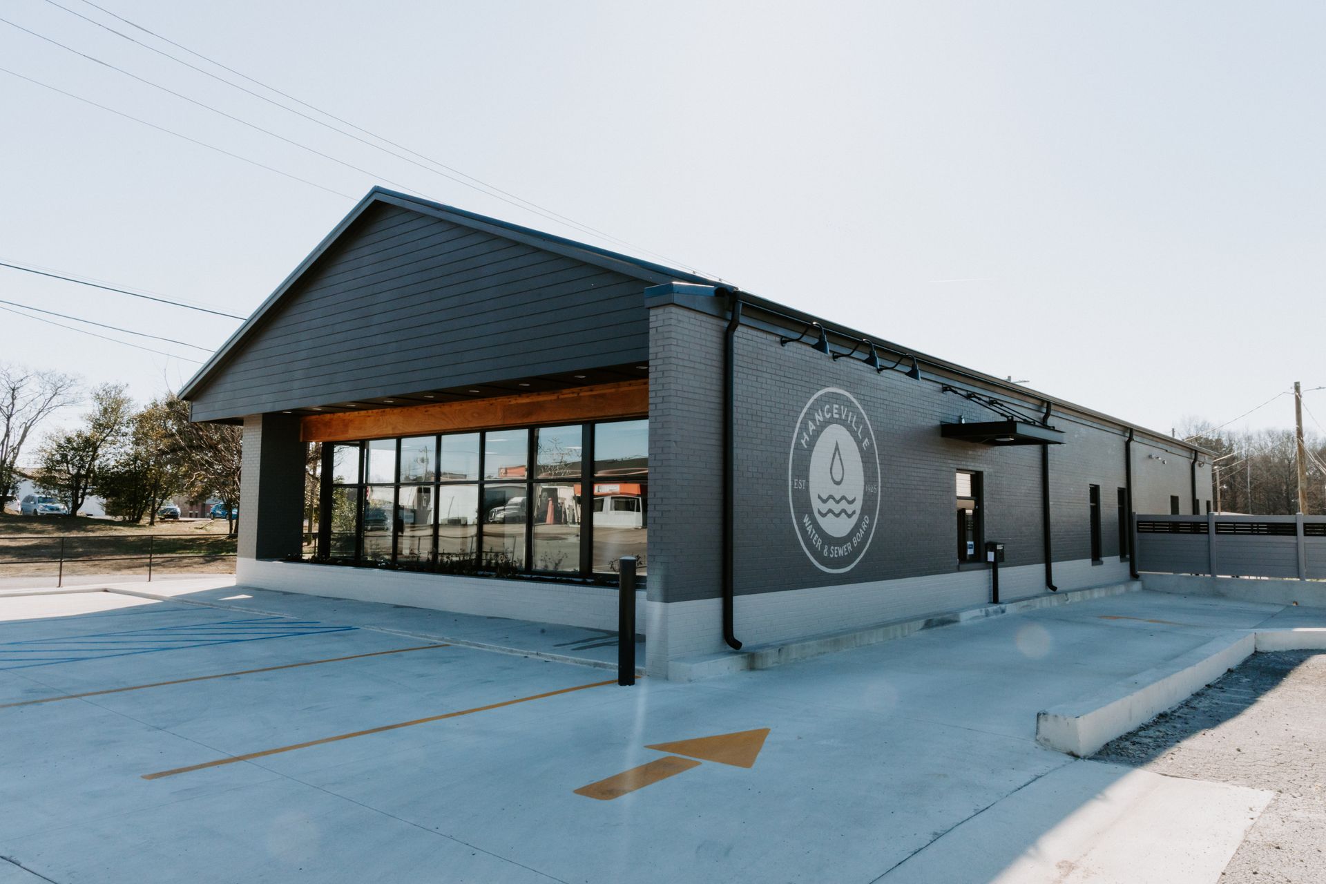 Exterior view of a modern building with dark gray siding and roof, long windows, and a concrete ramp under a cloudy sky.
