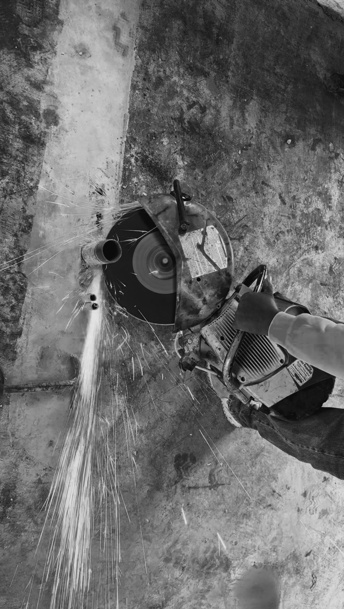 Person using a circular saw to cut concrete, sparks flying, gray tones.