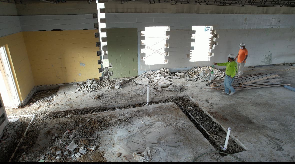 Interior construction scene; workers in a room with exposed walls and floor trenches.