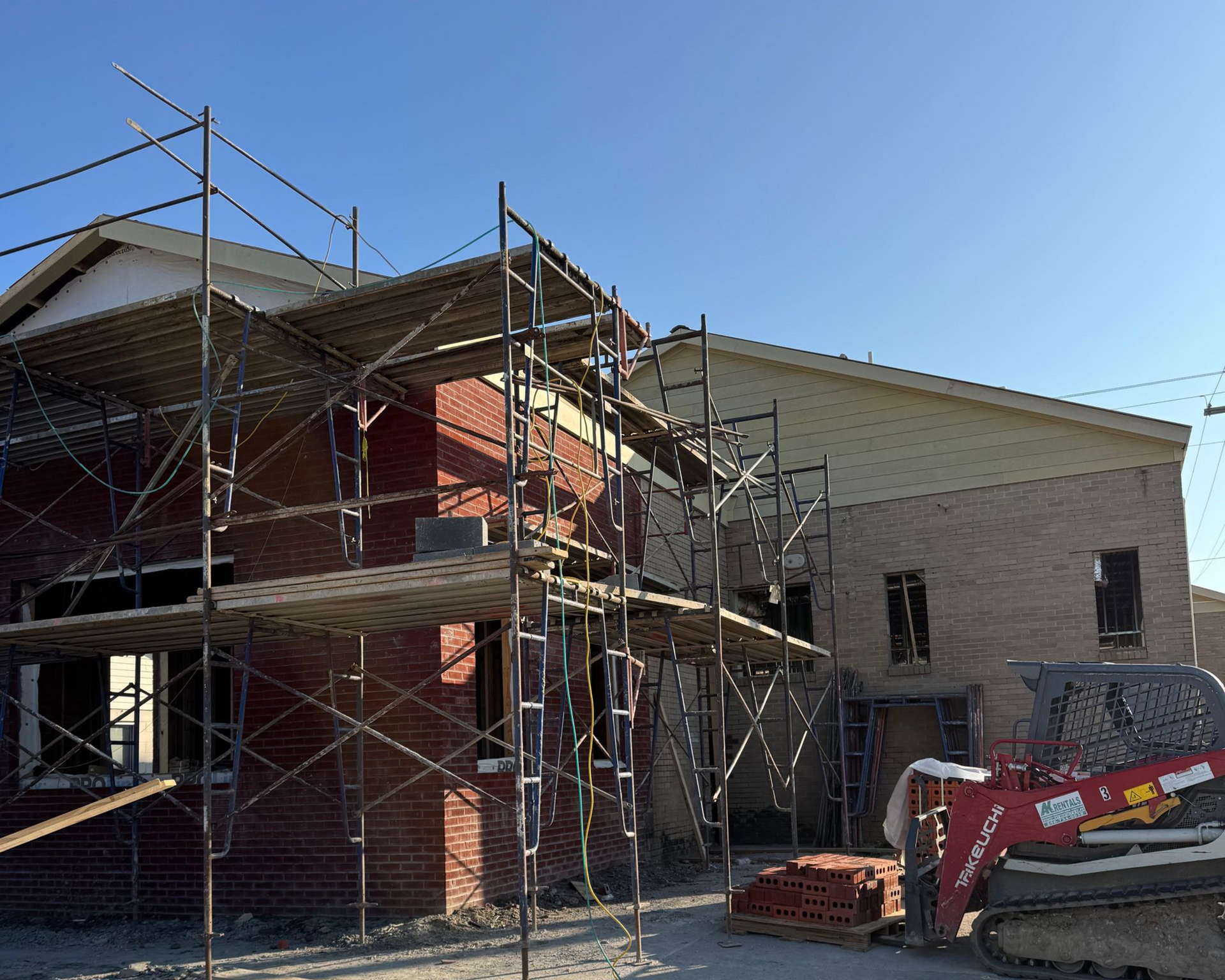 Construction site of a brick building with scaffolding, a small bulldozer, and a clear blue sky.