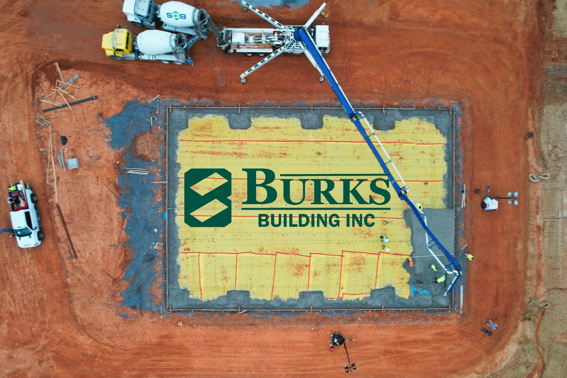 Aerial view of a construction site. Concrete being poured with Burks Building Inc. logo in the middle.