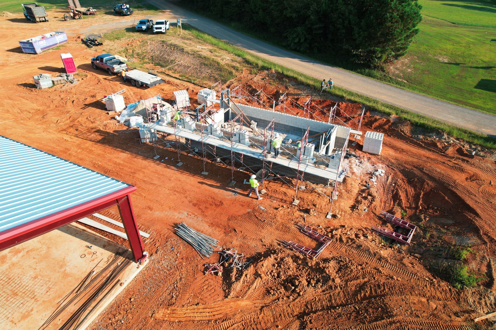 Construction site: a rectangular concrete structure with equipment, surrounded by red dirt.
