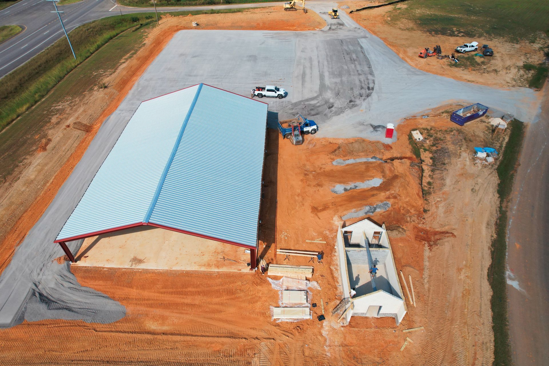 Aerial view of a metal-roofed building and construction site with red clay soil.