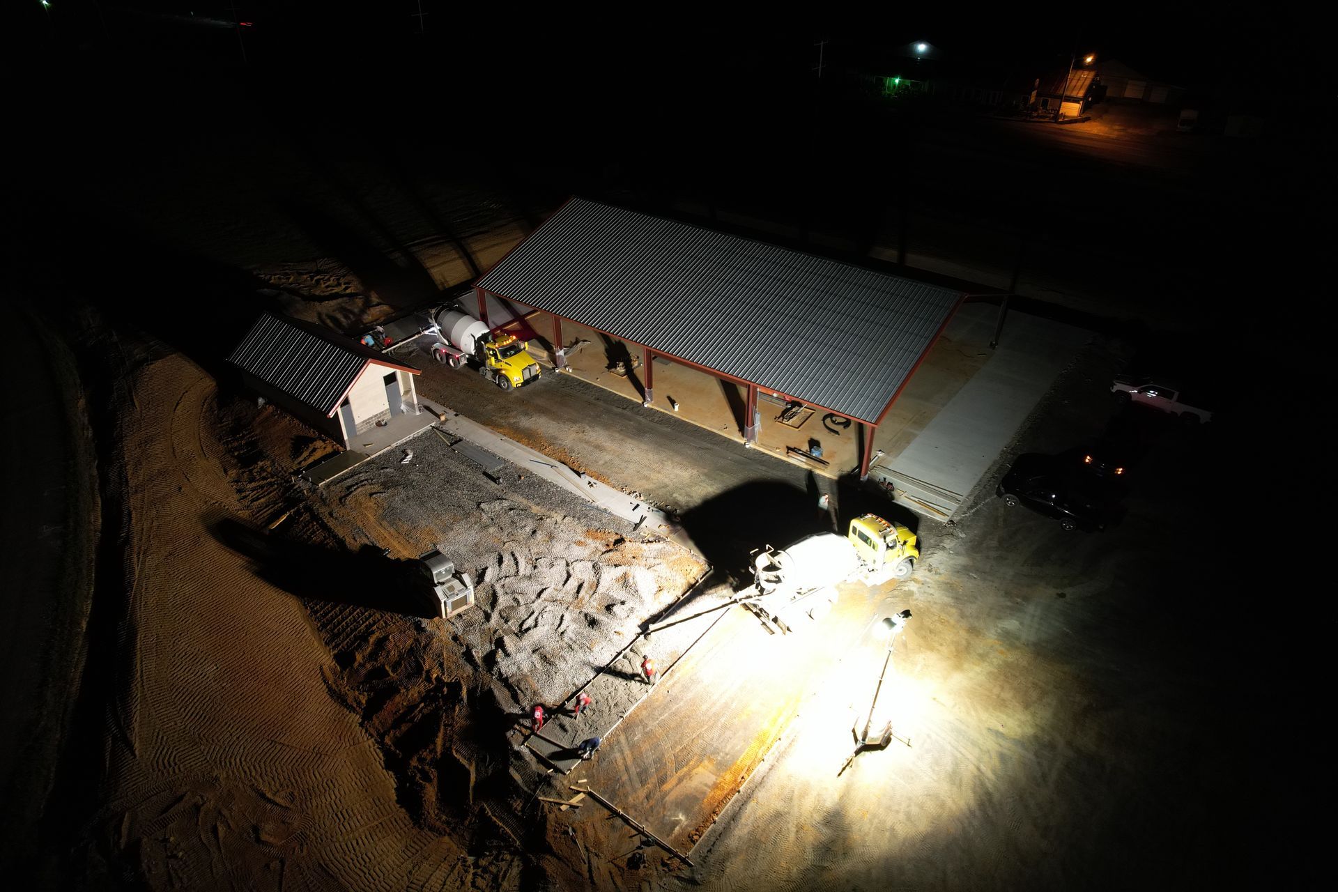 Night aerial view of an industrial site with bright lights illuminating equipment and buildings.