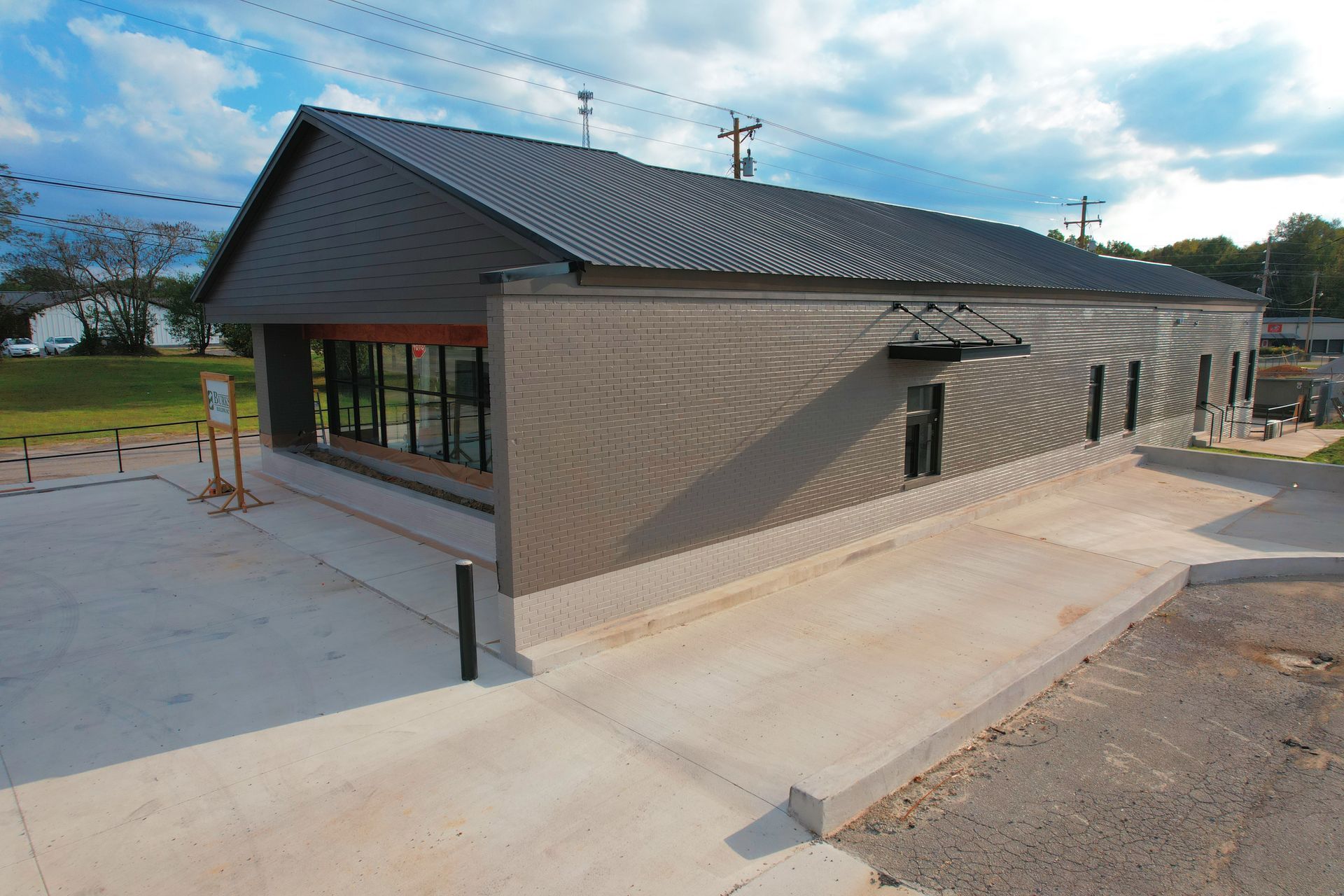 Exterior view of a modern building with dark gray siding and roof, long windows, and a concrete ramp under a cloudy sky.