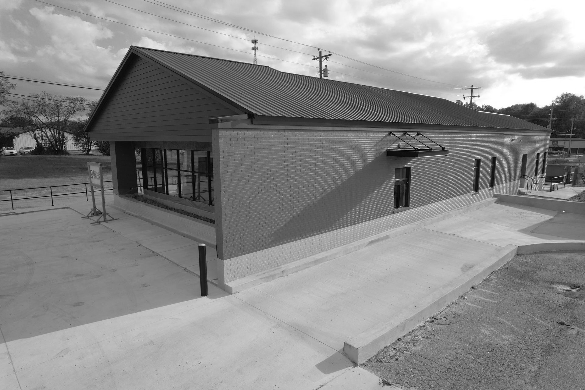 A gray-scale building with a sloped roof and a concrete ramp leading to the entrance.