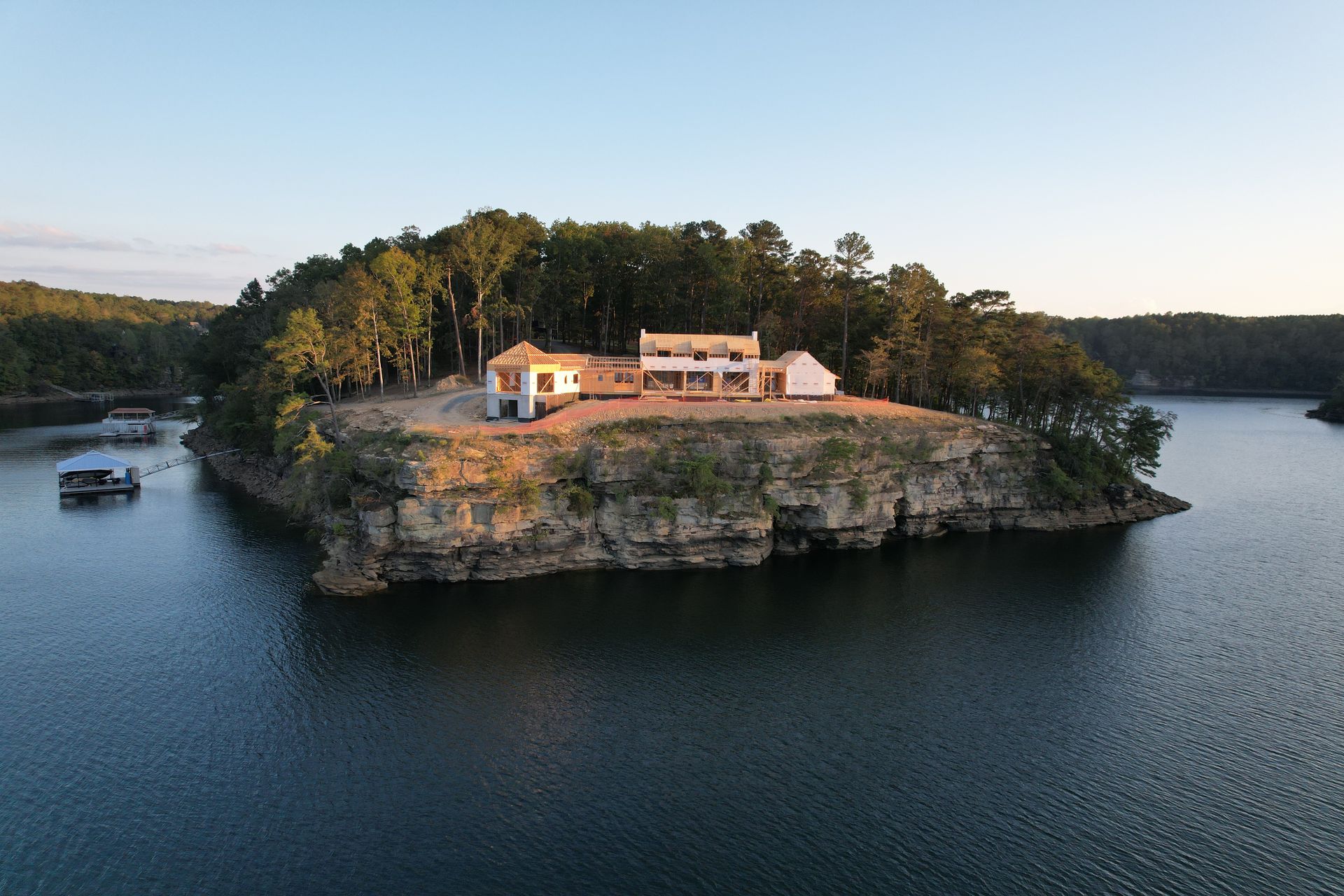 House on a small island overlooking a lake; trees and a houseboat visible.