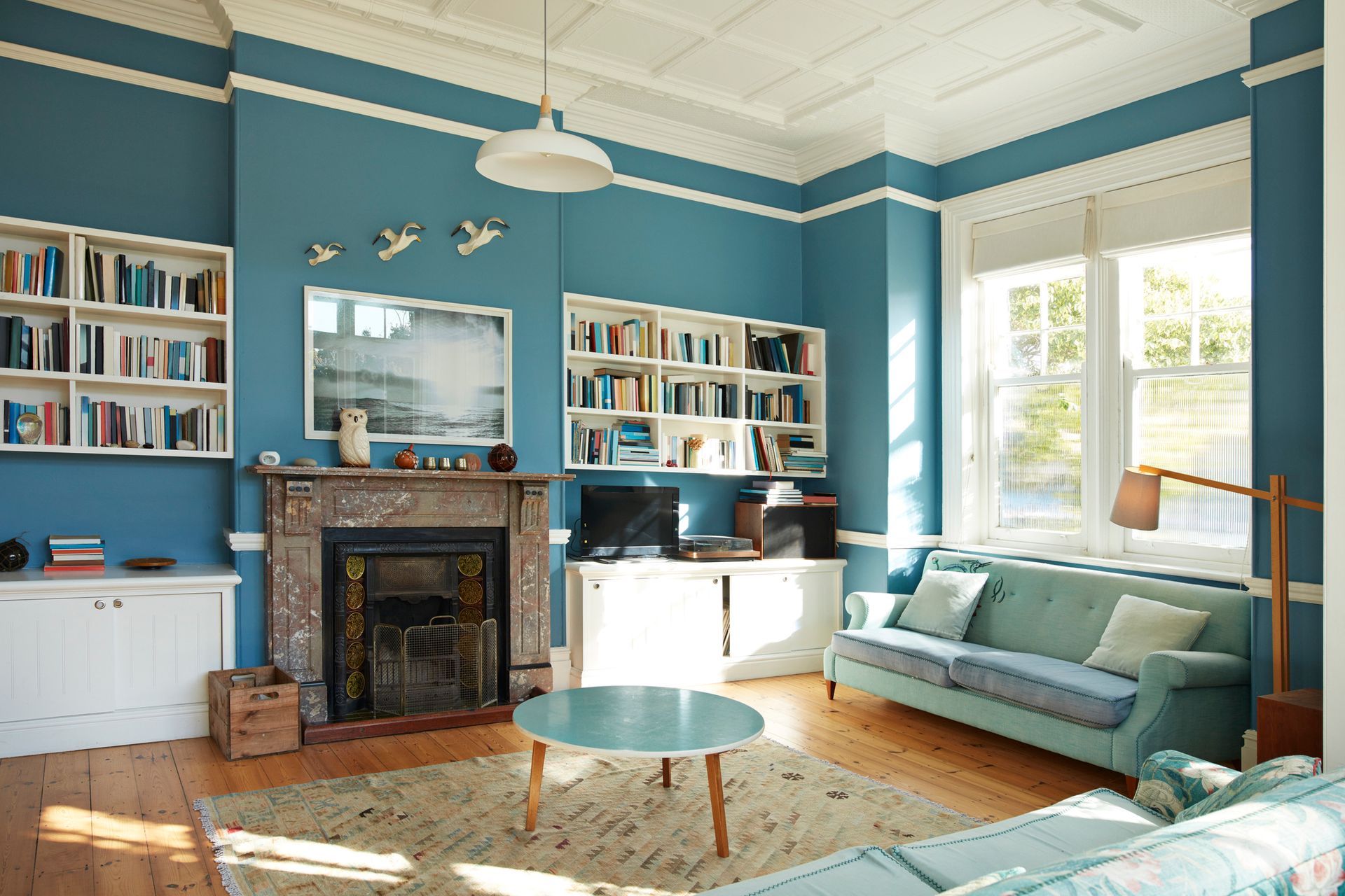 Blue living room with bookshelves, fireplace, and teal sofa.