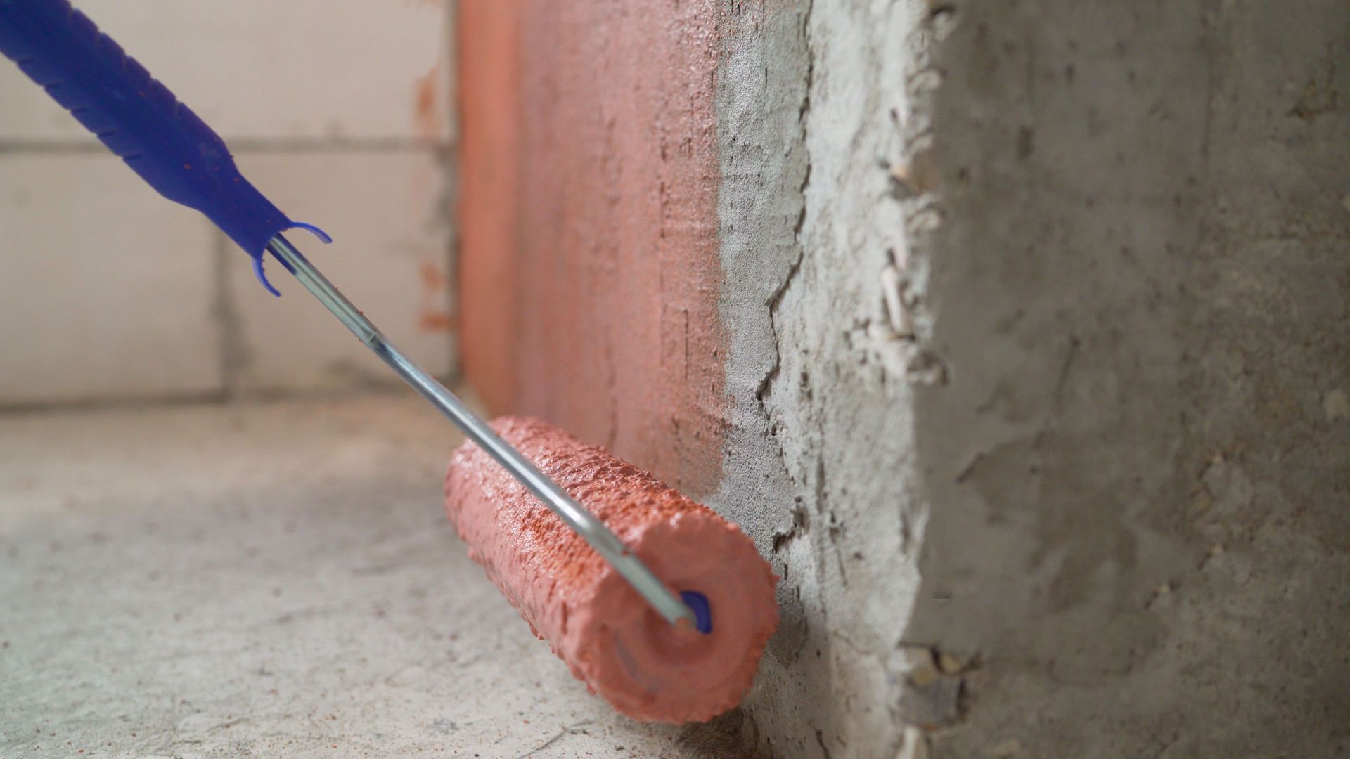 A person rolling orange sealant onto a concrete wall corner with a blue-handled roller.