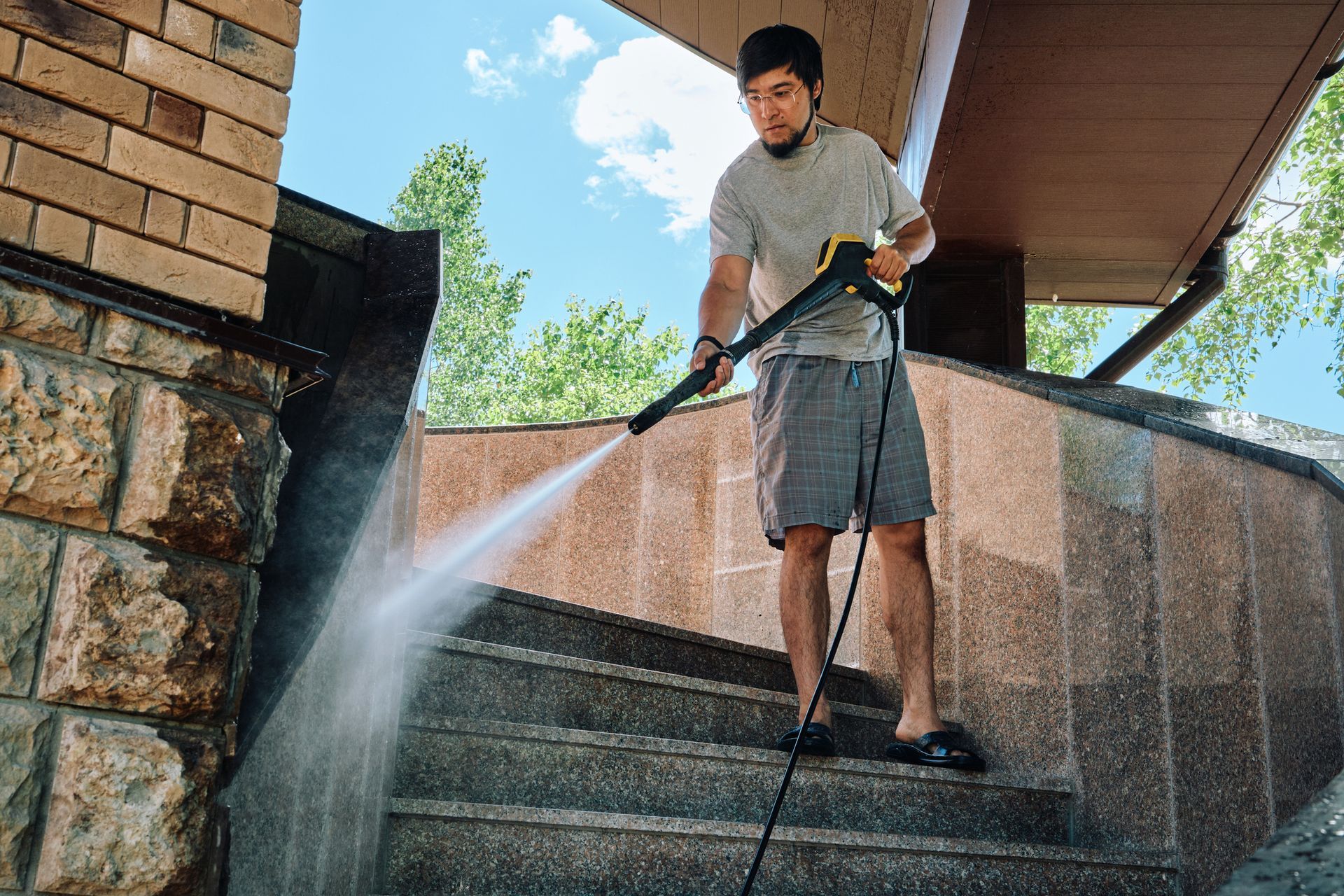 Man pressure washing stone steps outdoors.