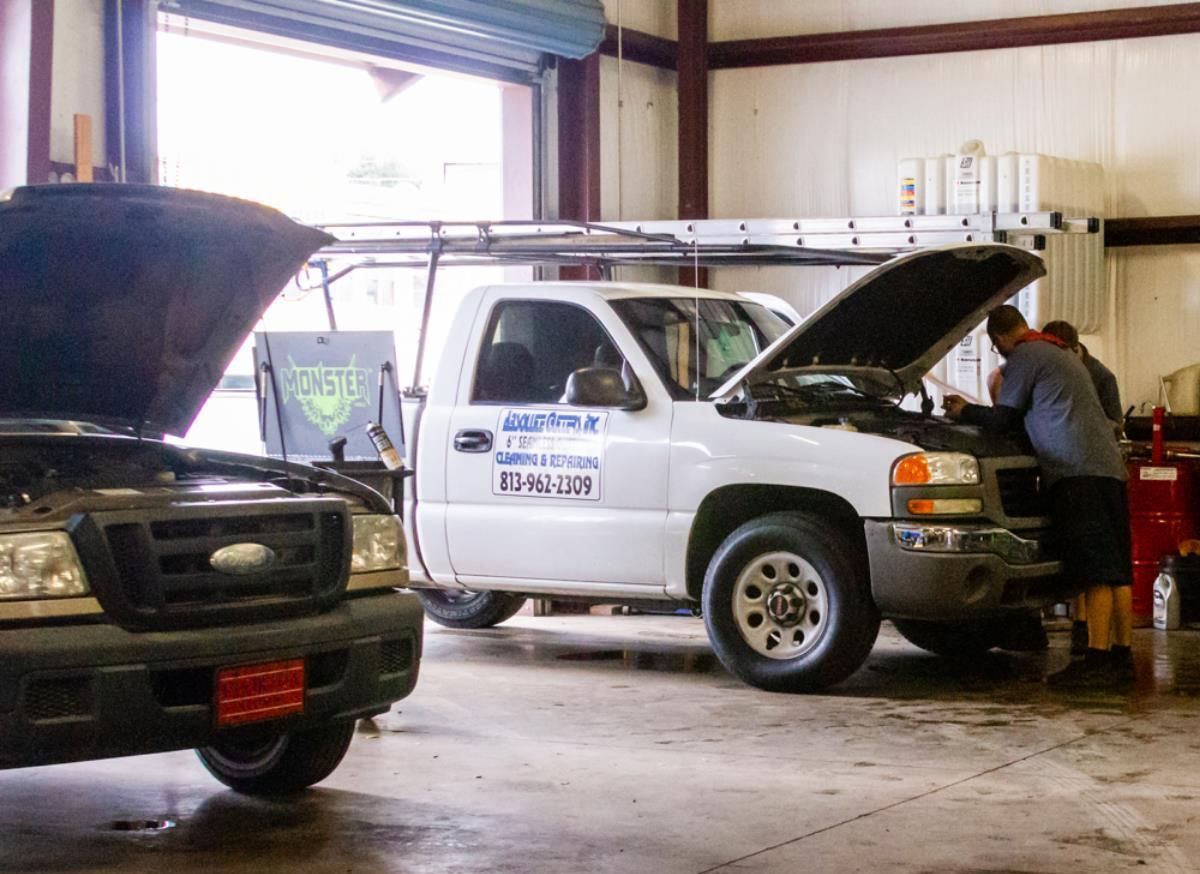 Two trucks are in a garage with their hoods open