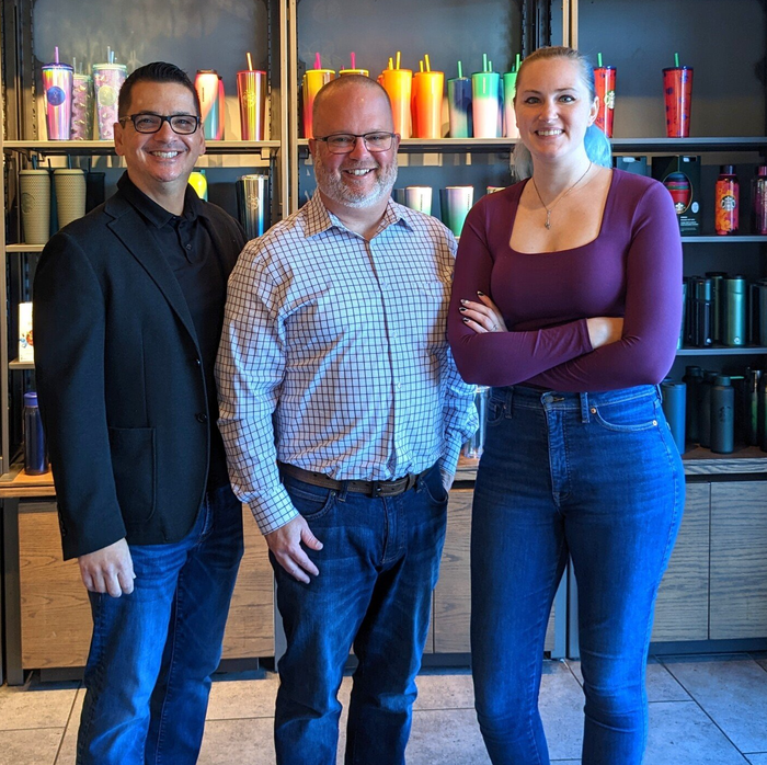 Three people posing for a picture in front of a shelf full of coffee cups