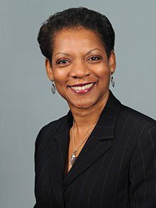 a woman in a black suit and earrings is smiling for the camera .