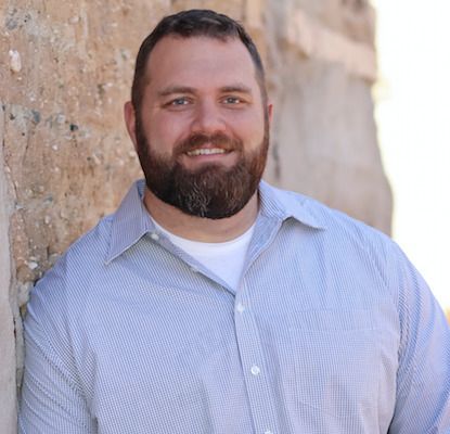 a man with a beard is leaning against a wall and smiling .