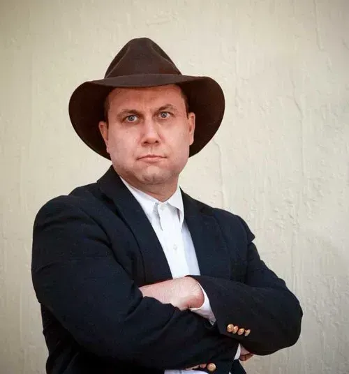 a man in a suit and cowboy hat stands with his arms crossed