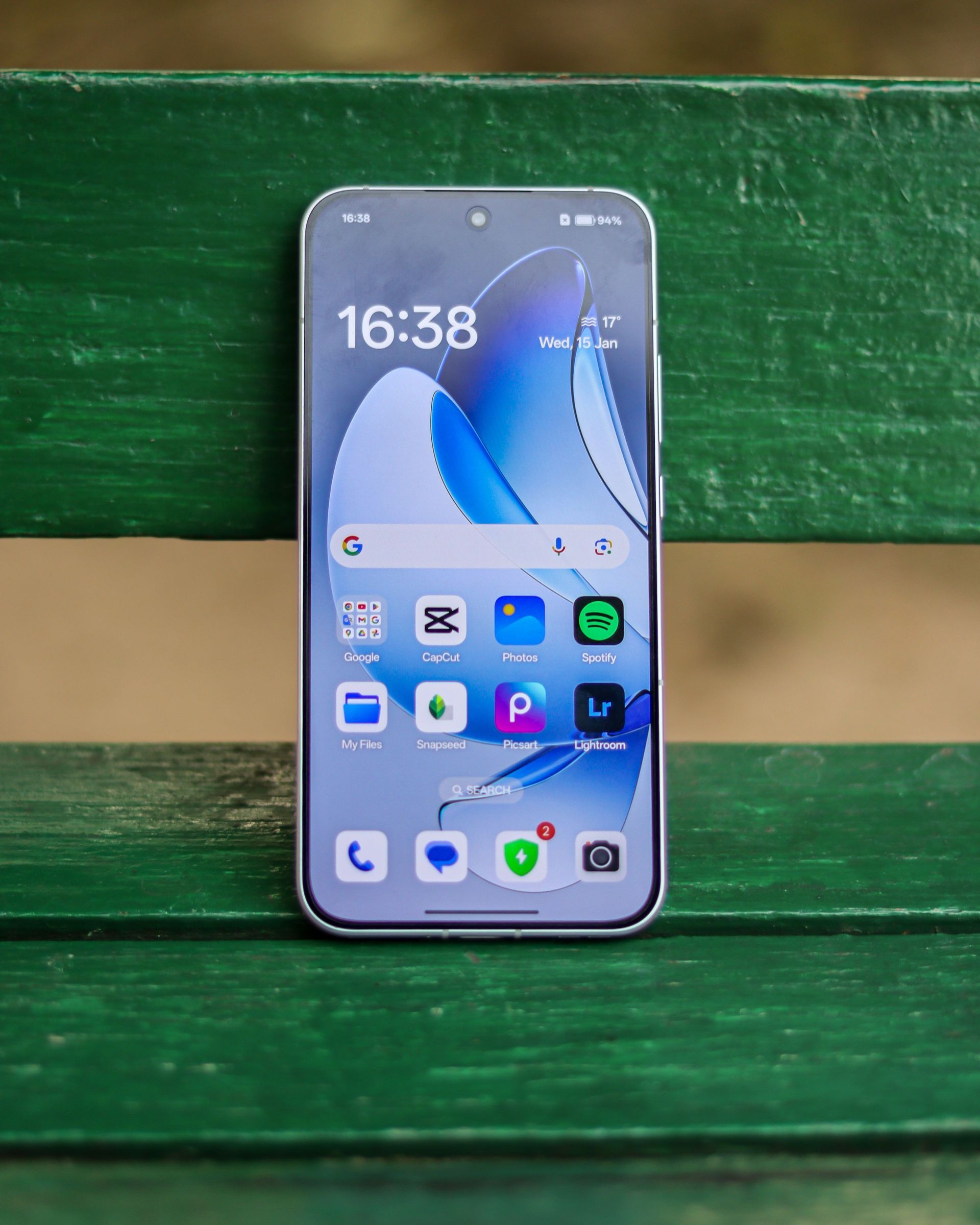 Smartphone standing on a green wooden bench, showing its home screen.