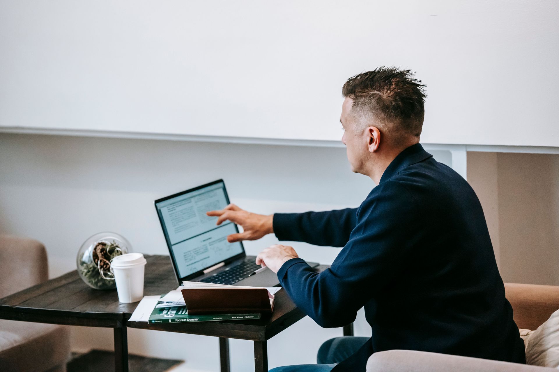 Person working on a laptop at a desk, pointing at the screen in a bright office.