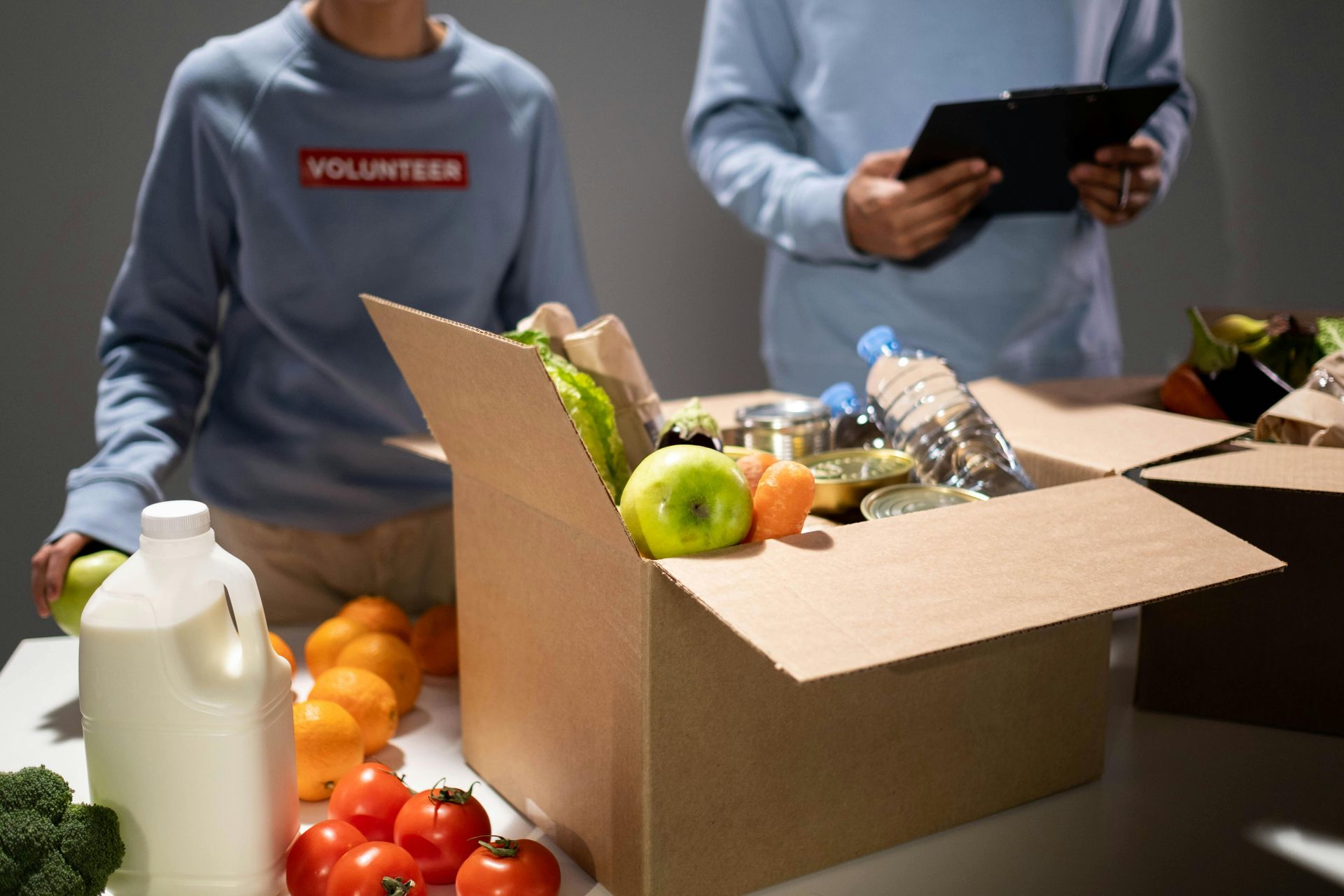 A man and a woman are standing next to a cardboard box filled with fruits and vegetables.