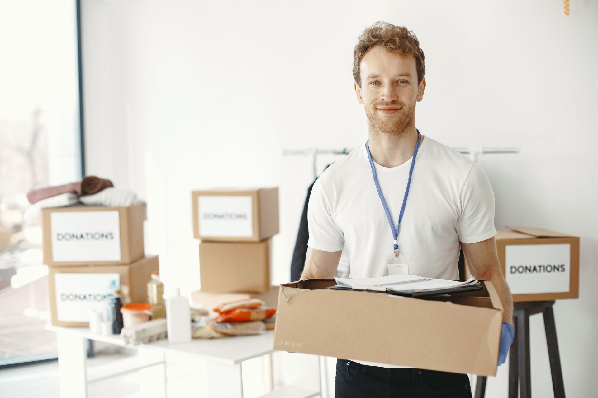Volunteer holding a donation box in a bright room with donation bins behind him