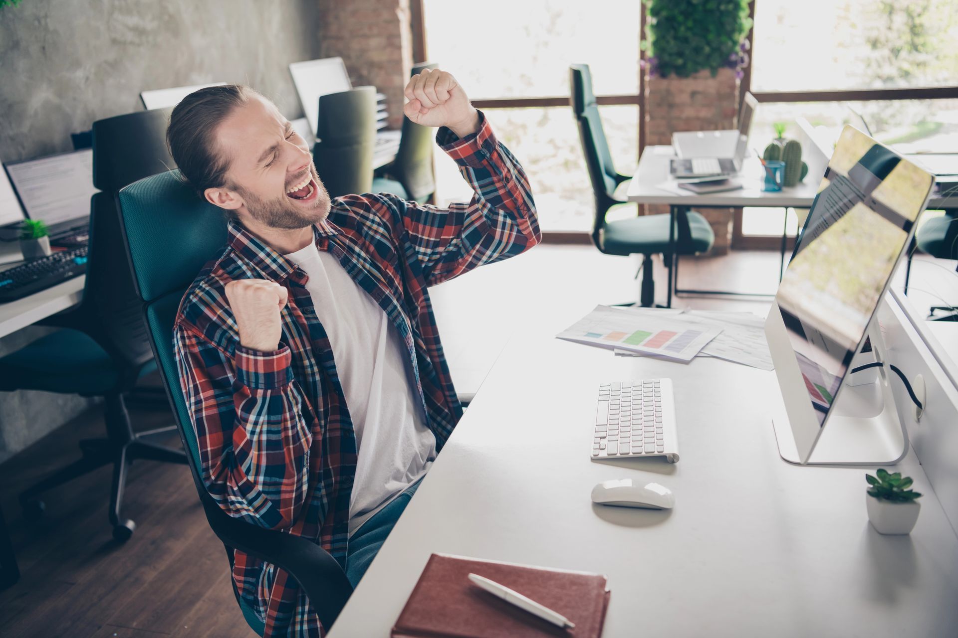 A man is sitting at a desk in an office with his arms in the air.