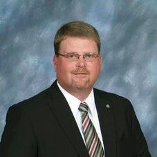 A man in a suit and tie is standing in front of a blue background.