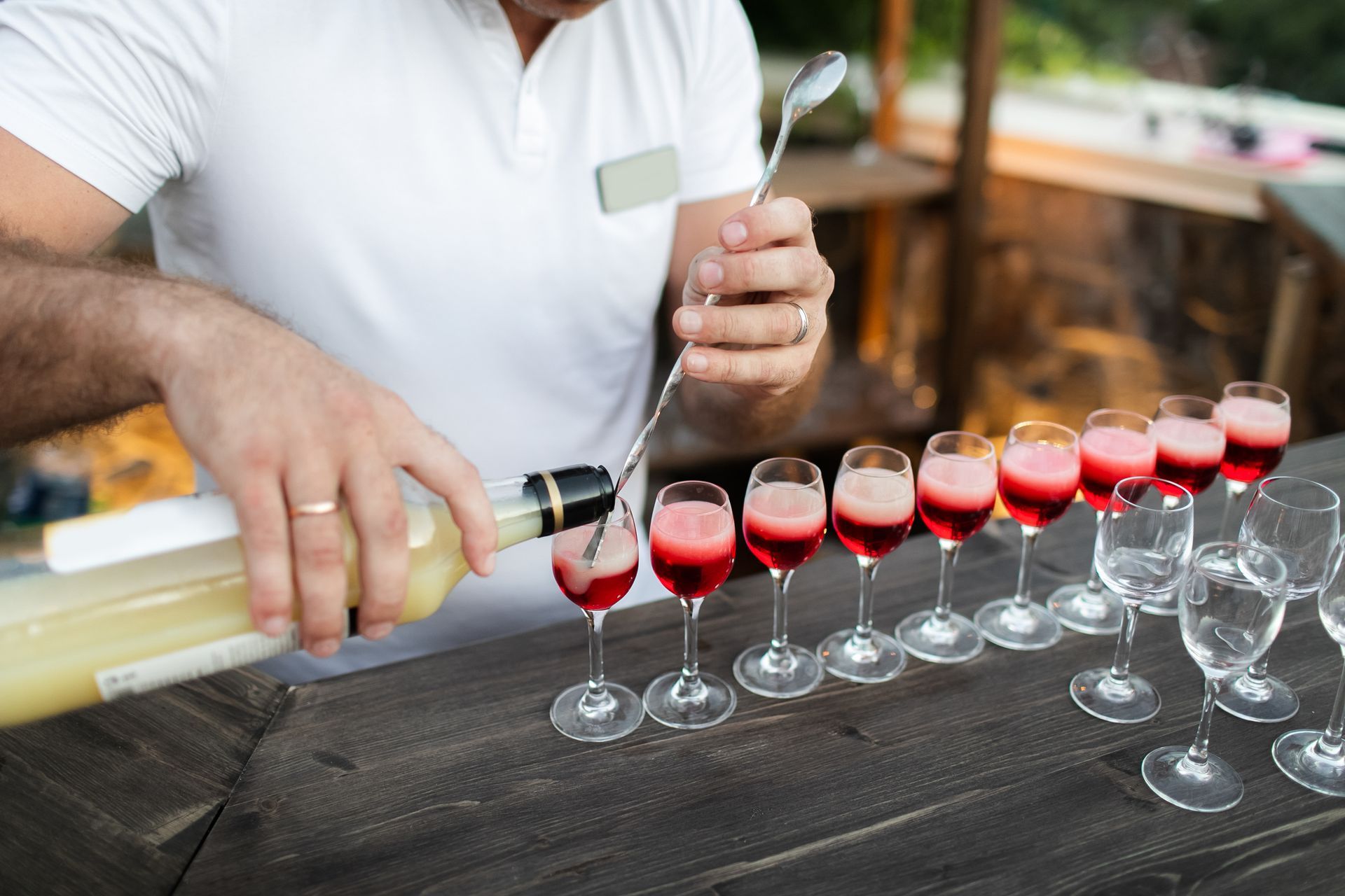 A man is pouring wine into a row of wine glasses.