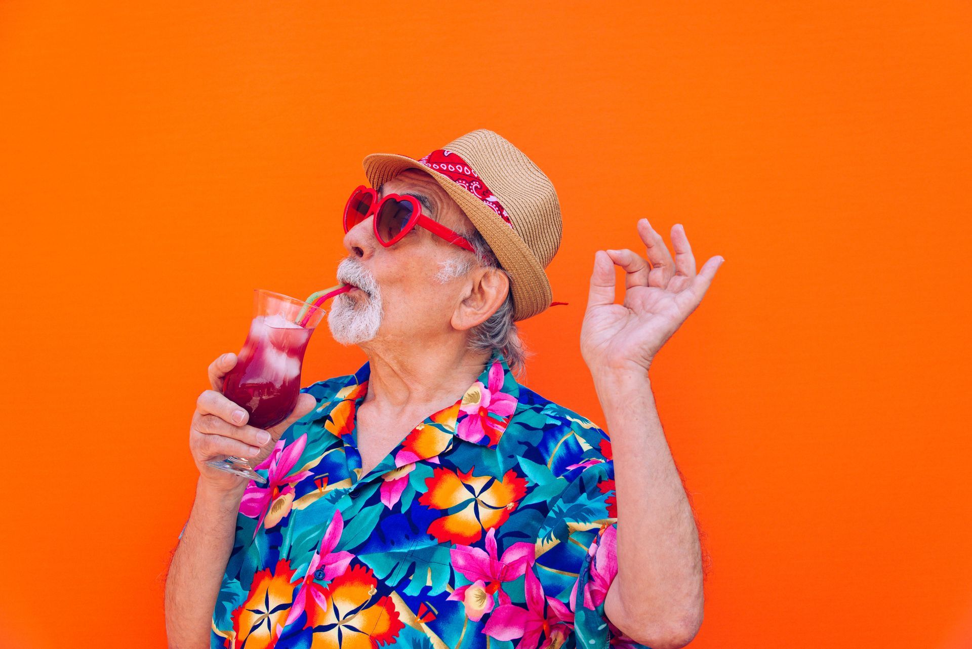 An elderly man is drinking a cocktail through a straw.