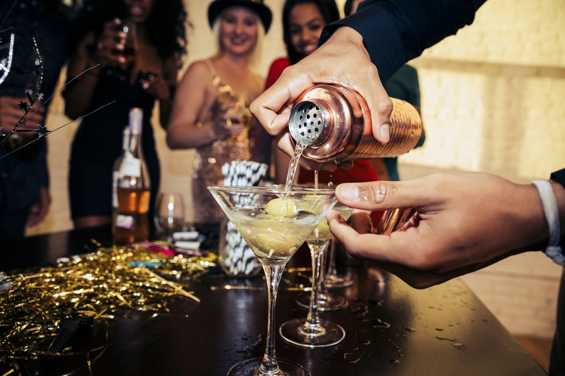 A man is pouring a martini into a martini glass at a party.