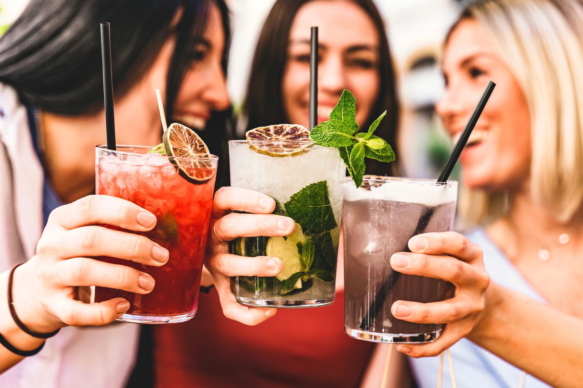 A group of women are holding up glasses of drinks with straws.