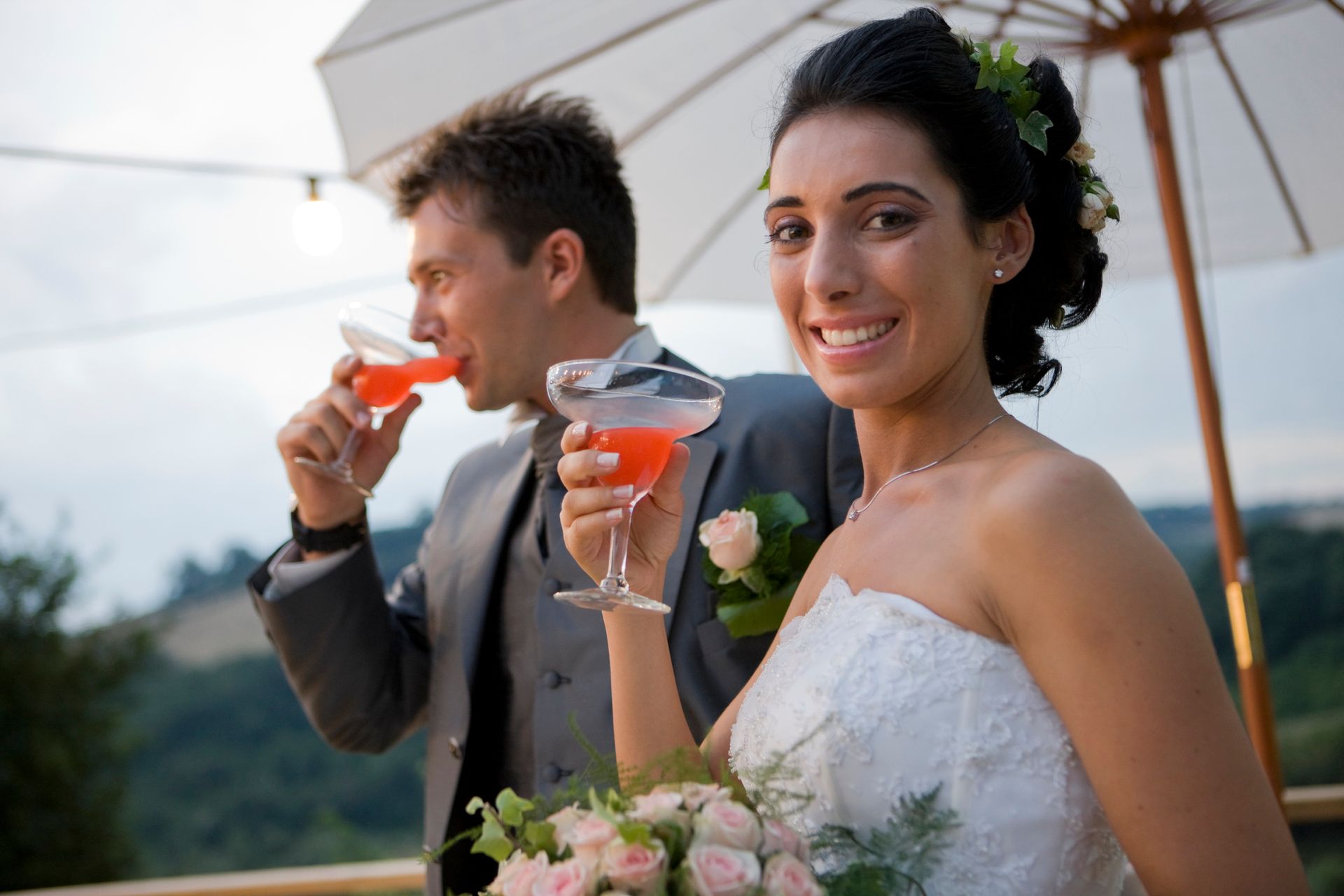 A bride and groom drinking cocktails under an umbrella