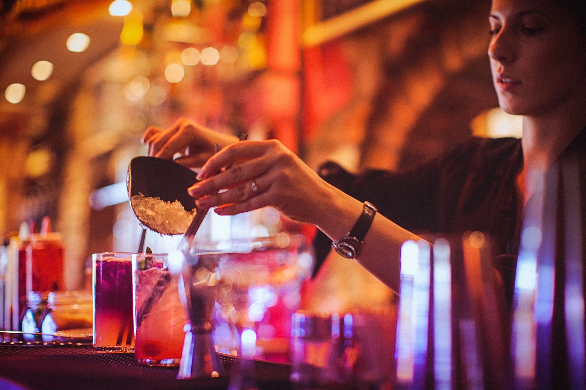 A woman is pouring a drink into a glass at a bar.