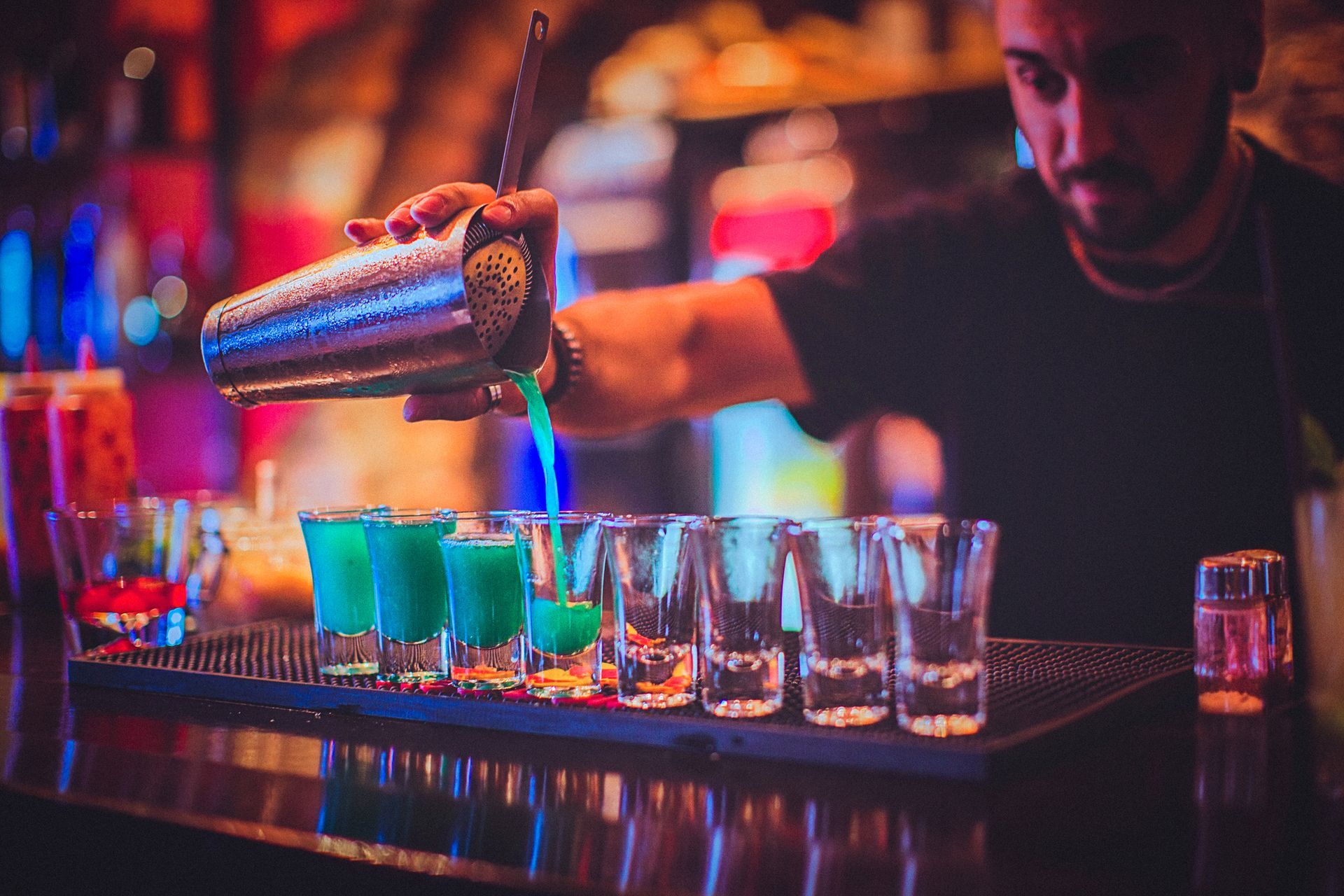 A bartender is pouring a drink into a row of shot glasses.