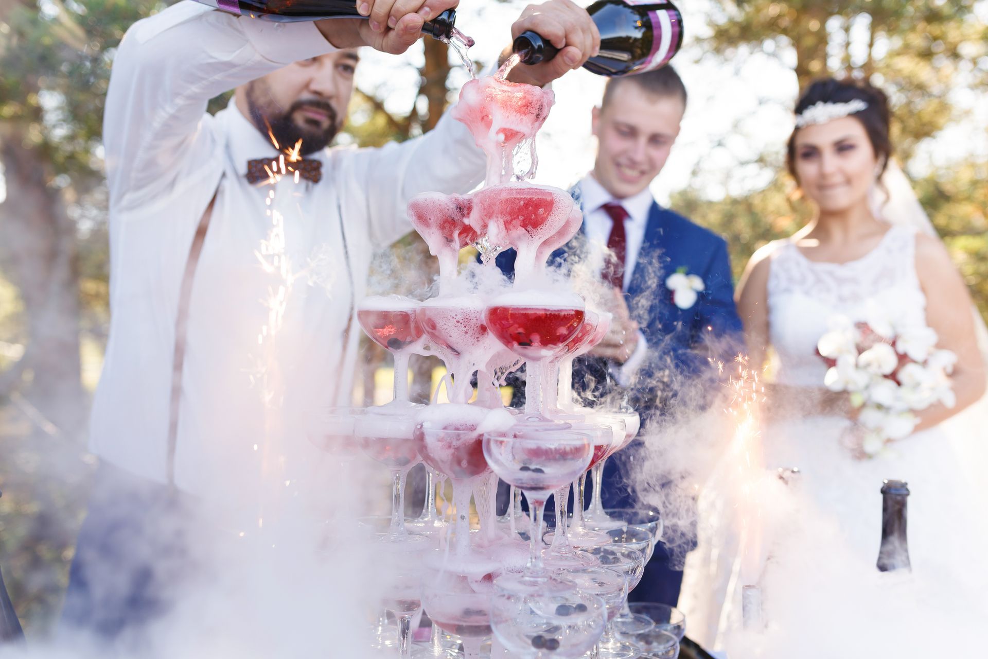 A man is pouring champagne into a pyramid of champagne glasses.