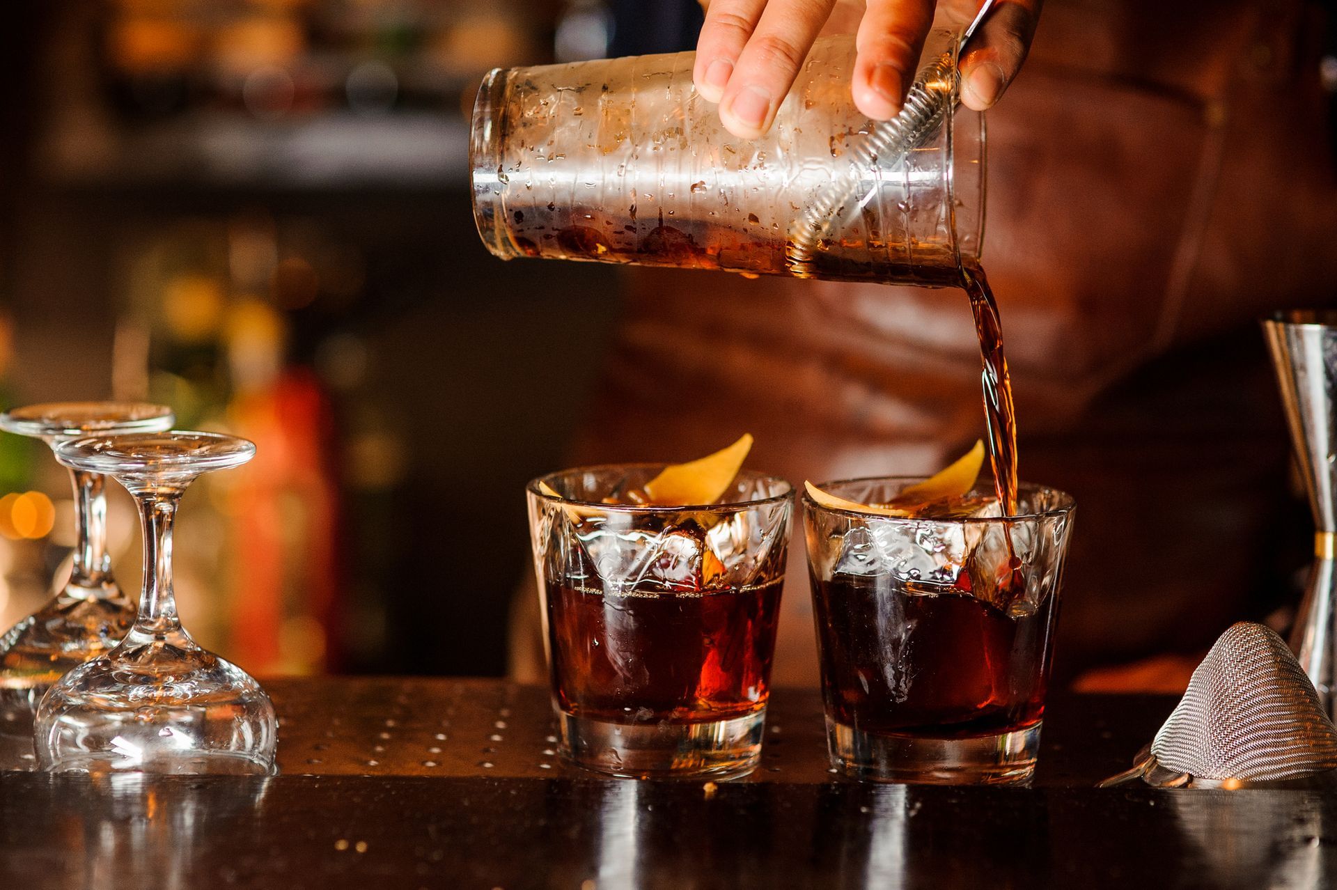 A bartender is pouring a drink into two shot glasses.