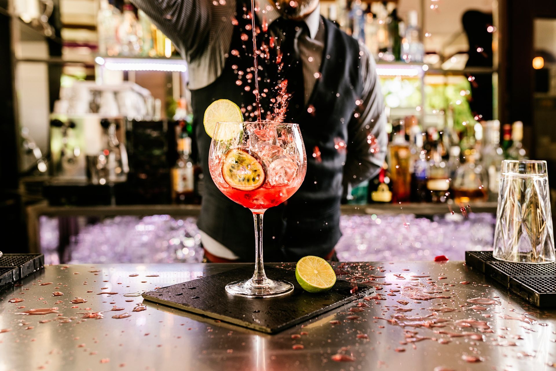 A bartender is pouring a drink into a glass on a bar.