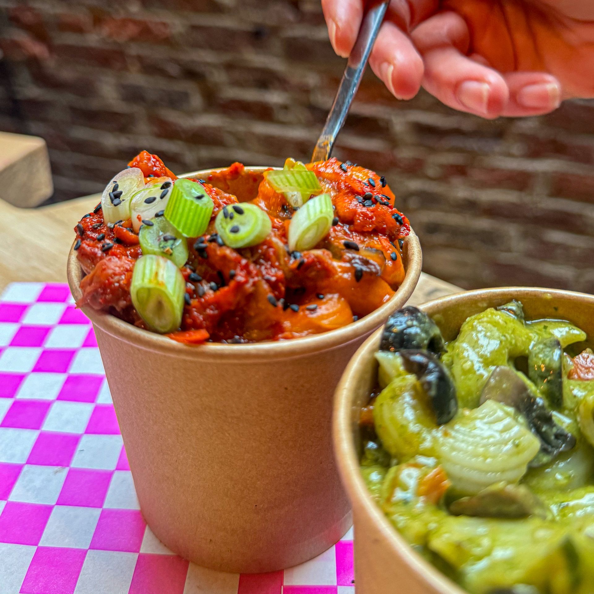 A person is dipping a spoon into a cup of food.