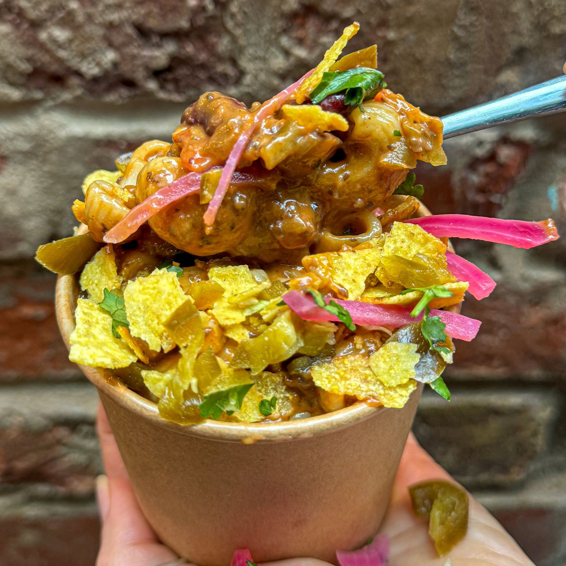 A person is holding a cup of food with a spoon in it.