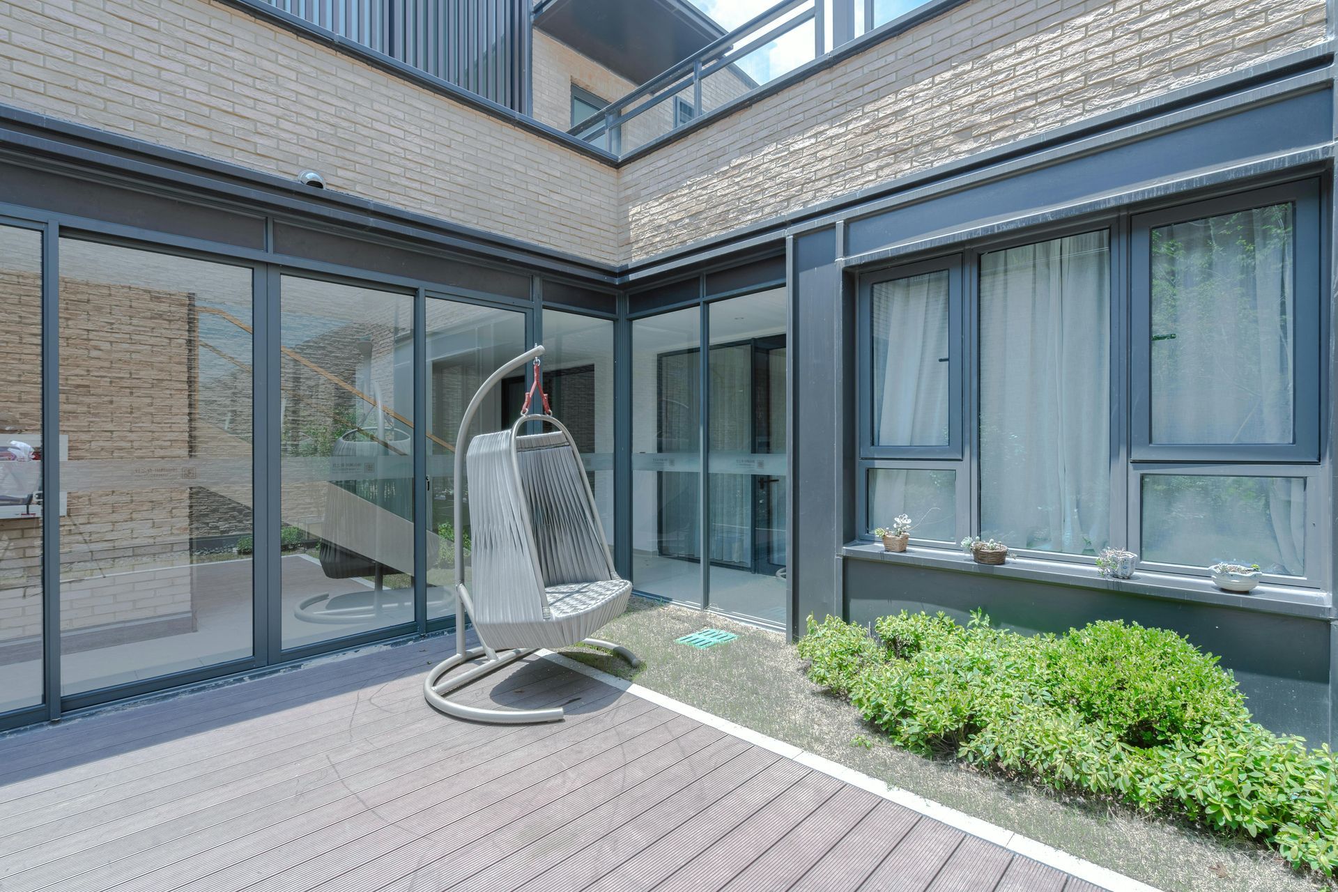 Une terrasse extérieure moderne avec un fauteuil suspendu, des portes coulissantes en verre et un petit carré de verdure.