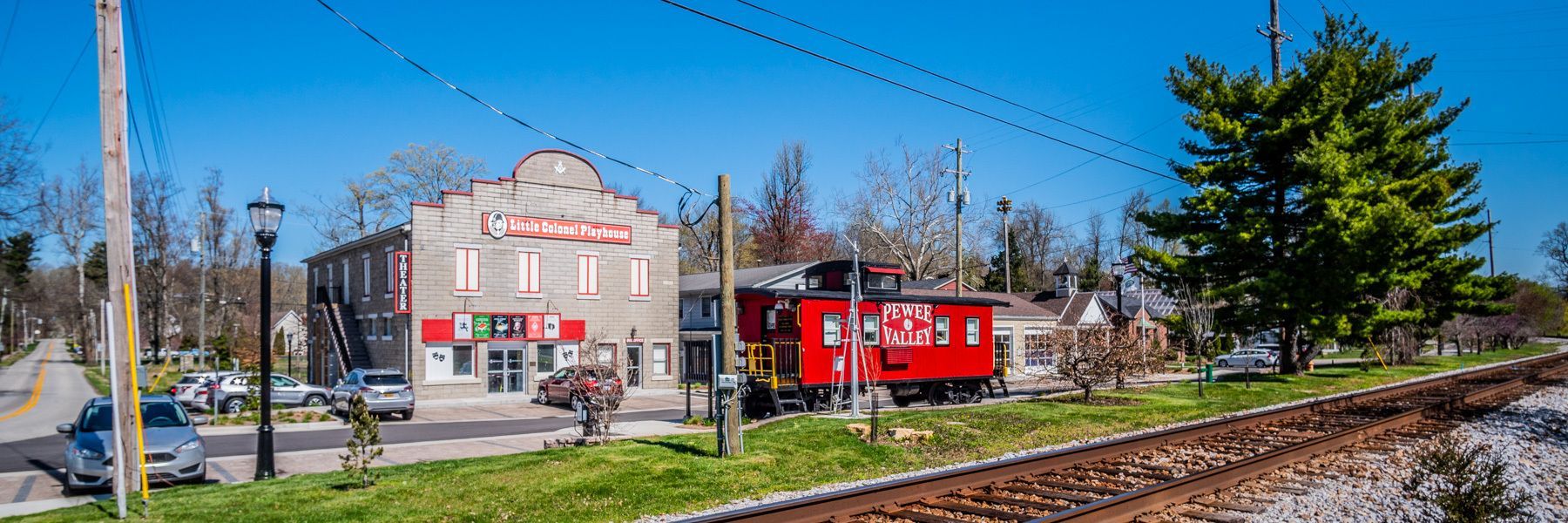 A red train car is parked on the tracks in front of a building.