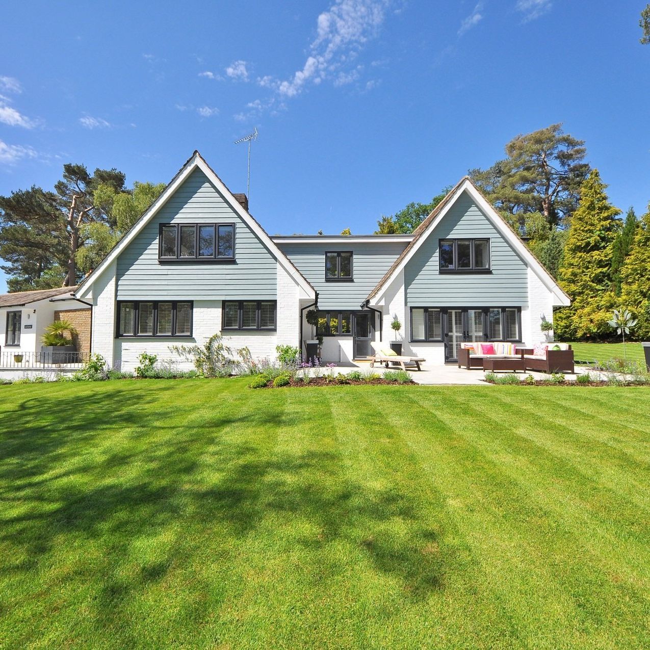 House with light blue and white exterior, two gabled sections, black framed windows, and a large green lawn under a blue sky.