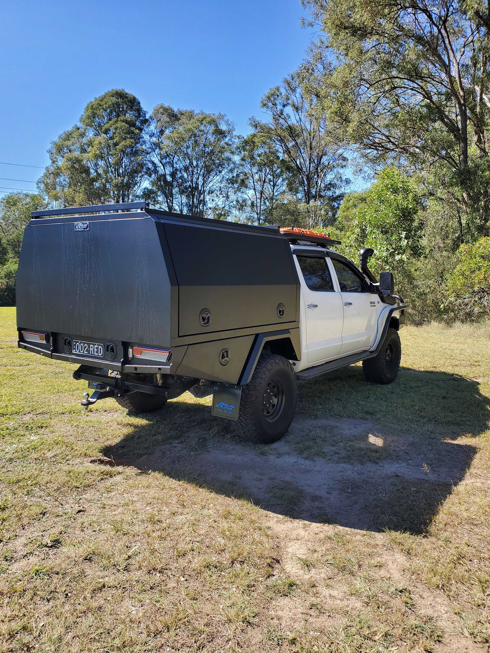 A white truck with a black canopy is parked in a grassy field.