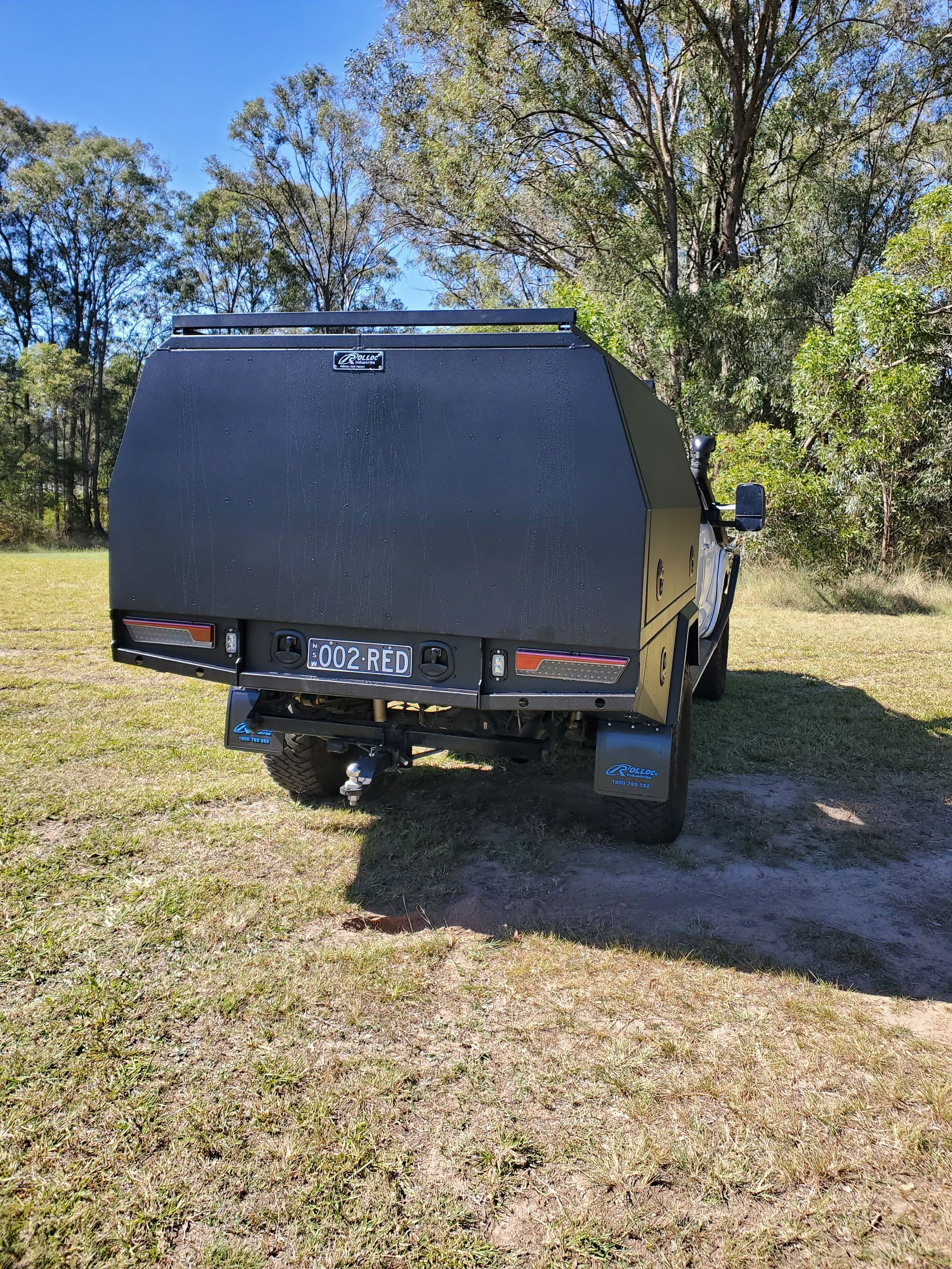 A black truck with a canopy is parked in a grassy field.