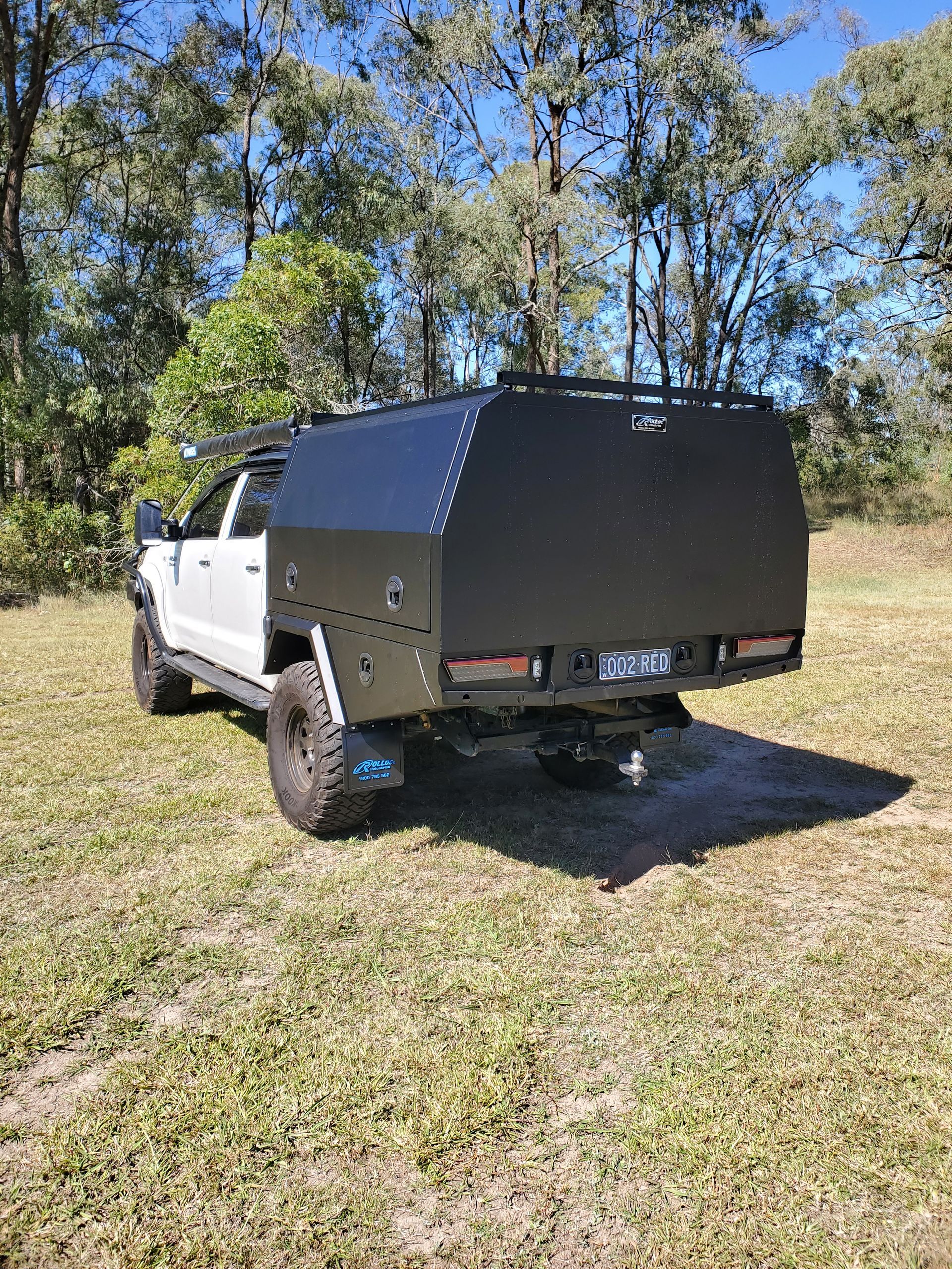A white truck with a black canopy is parked in a grassy field.