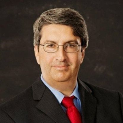 Man in glasses, suit, and red tie, smiling at the camera.