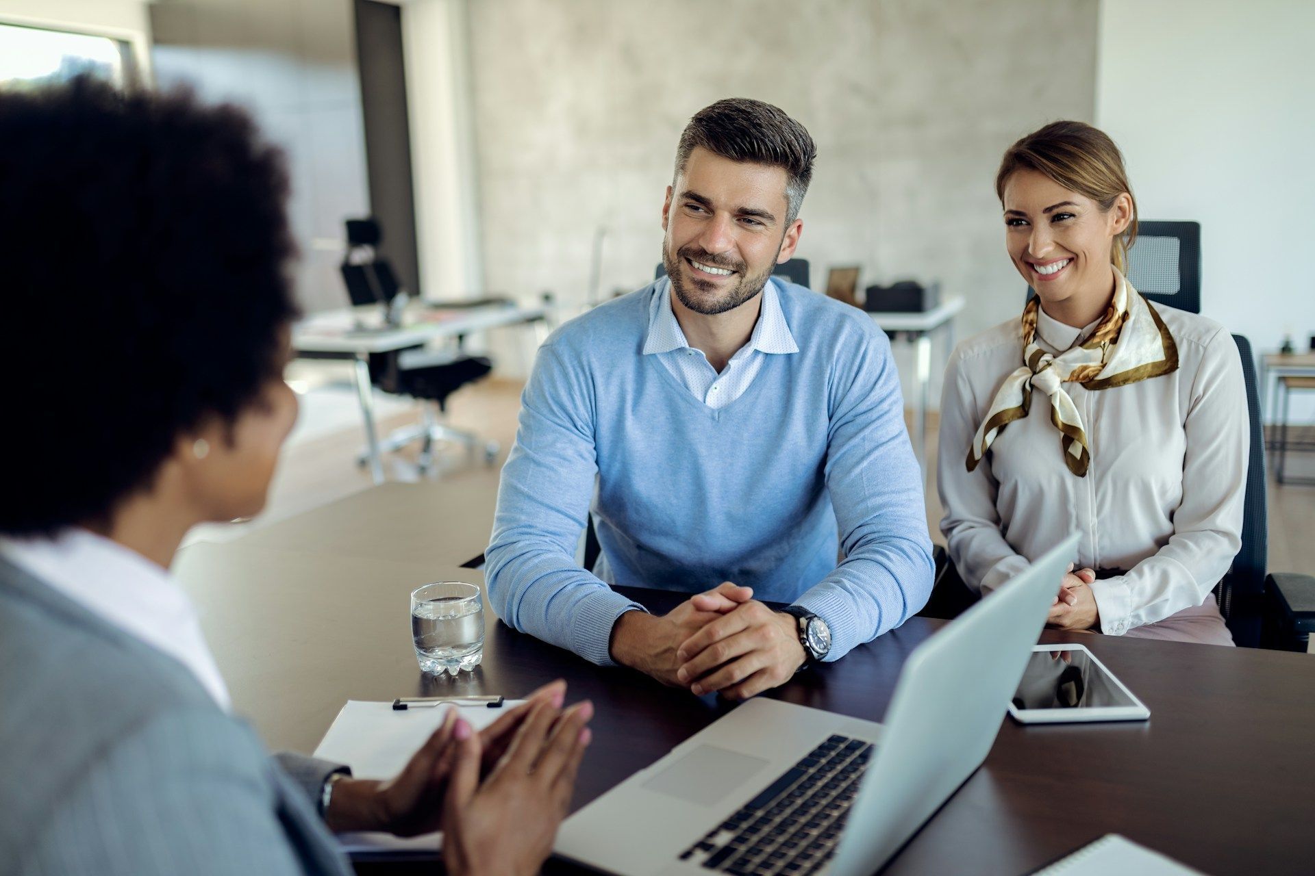 Woman advising a couple at a desk with a laptop, looking at them.