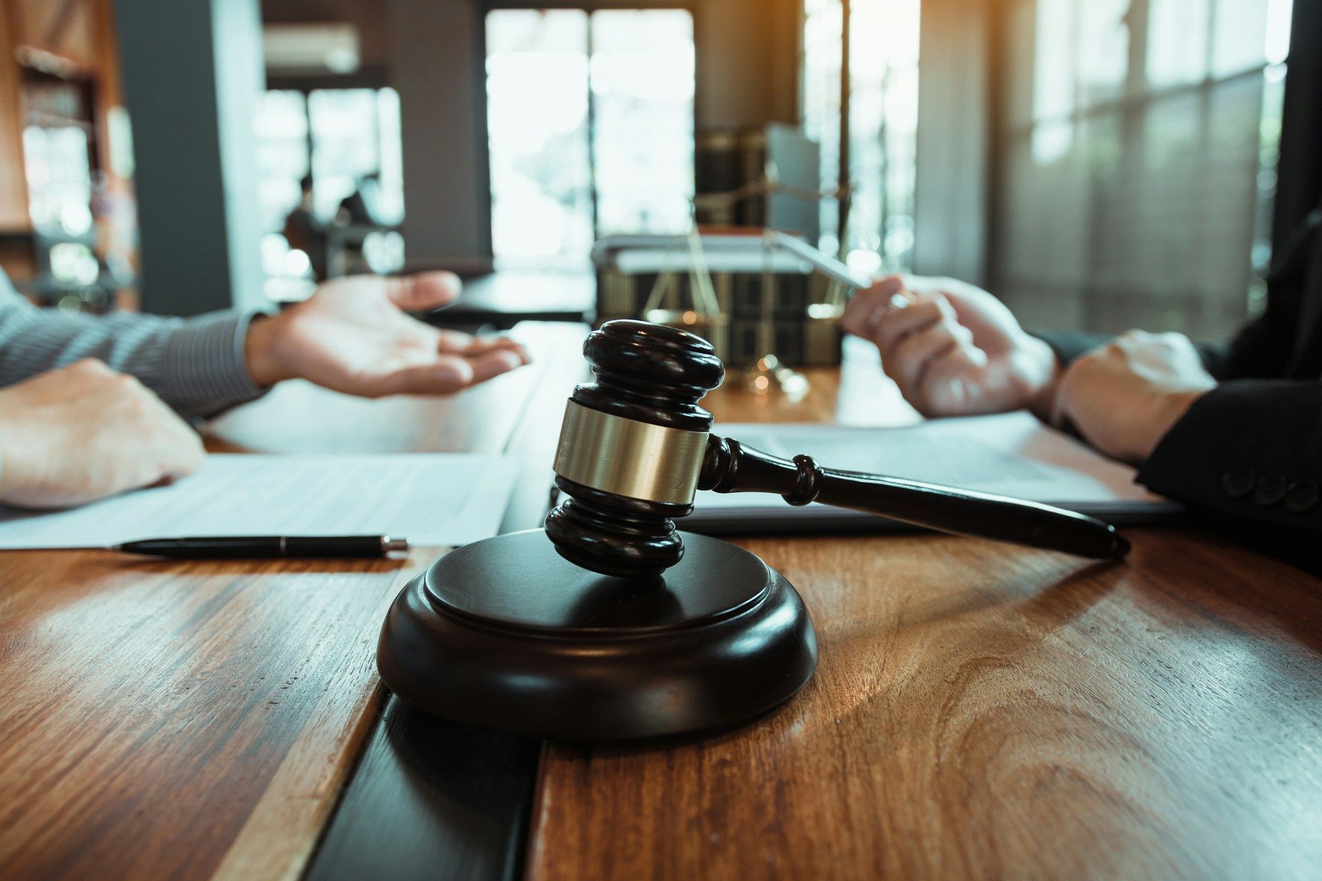 Gavel on a wooden table between two people; one gesturing, reviewing documents in an office setting.