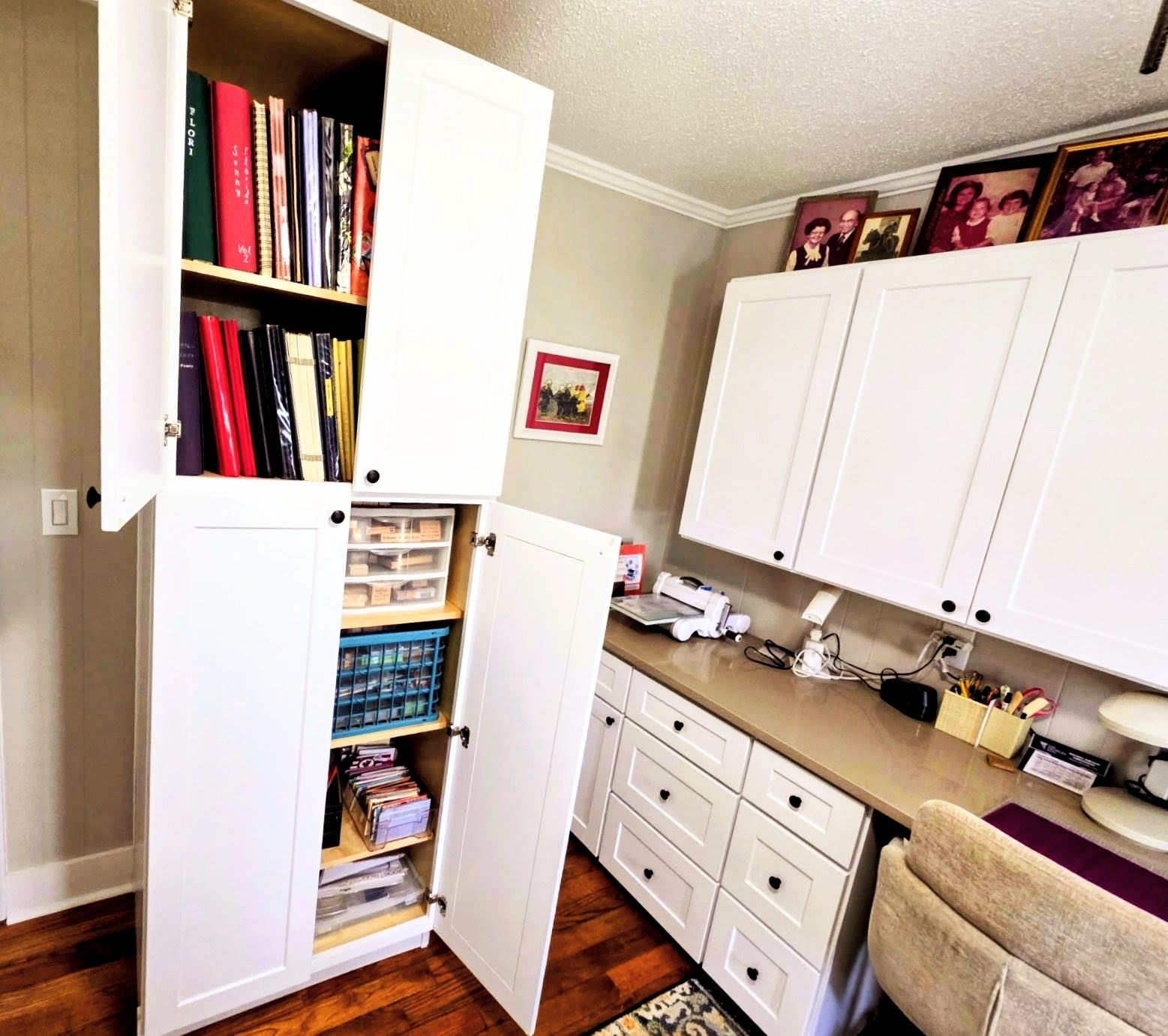 A well-organized craft room featuring a tall white cabinet filled with books and supplies, next to a white desk and cabinets.