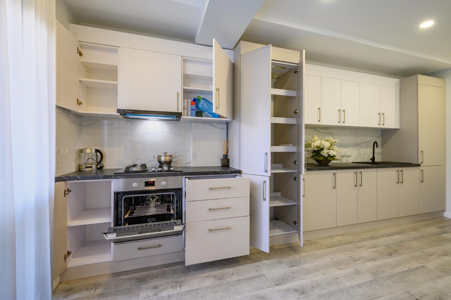 White kitchen with open cabinets, oven, and drawers, showing interior shelving, and a stovetop.