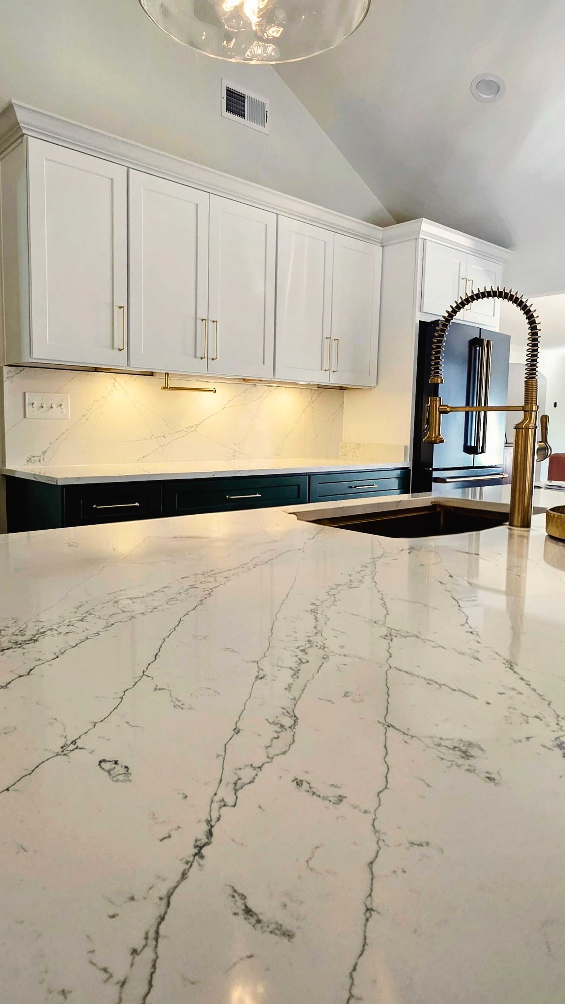 Kitchen with white cabinets, marble countertop, and gold faucet.